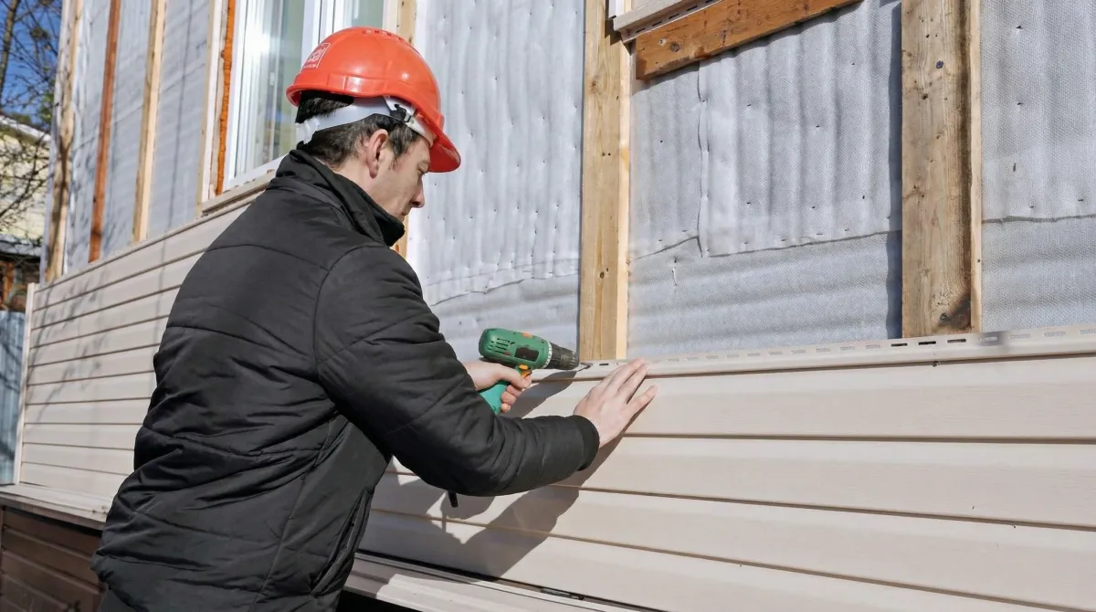 Siding replacement professional using a power drill to install new tan vinyl siding on a home exterior in West Palm Beach, FL